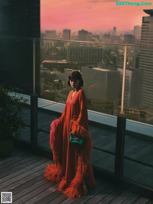 A woman in a pink dress sitting on the ground with a black bag.