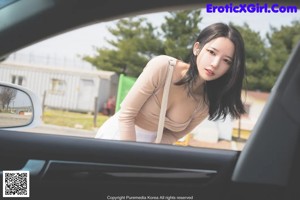 A woman in a white dress and high heels leaning out of a car.