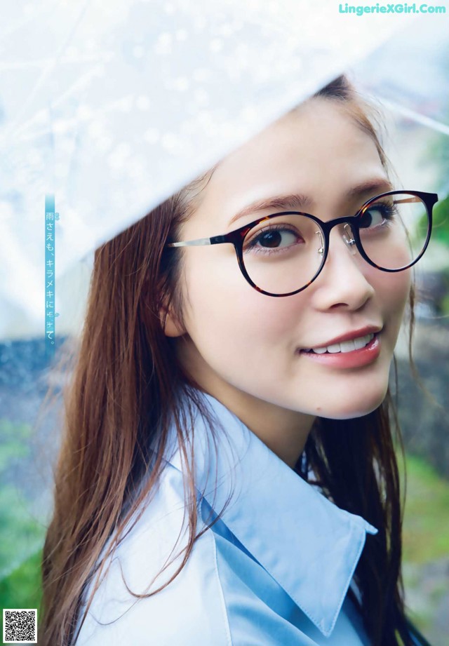 A woman wearing glasses and a blue shirt holding an umbrella.