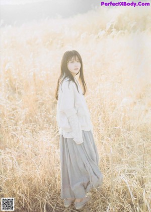 A woman in a yellow dress leaning against a tree.