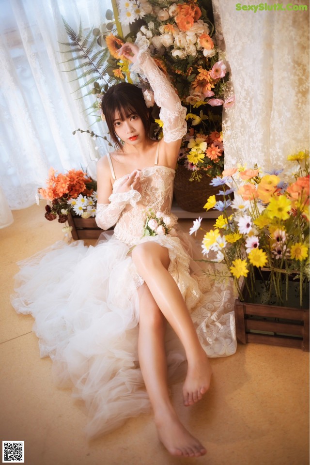 A woman in a white dress sitting on the floor next to flowers.