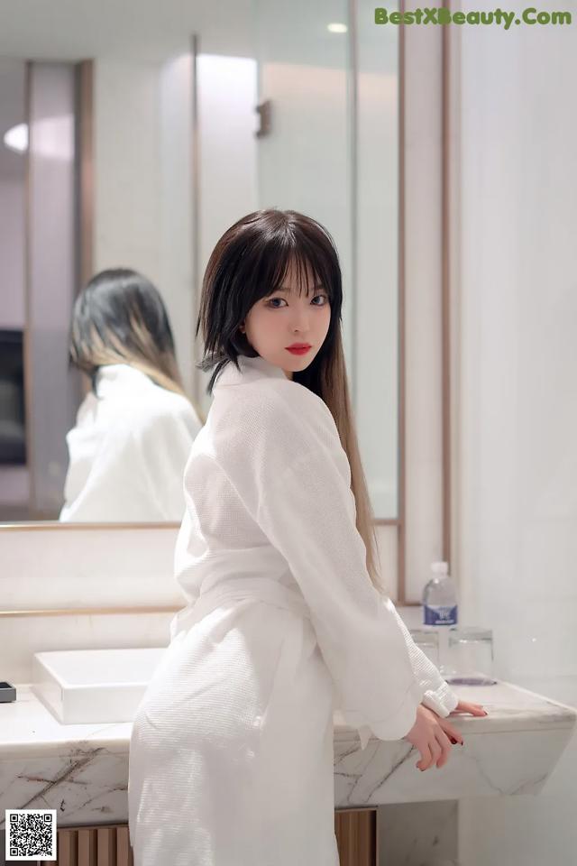 A woman in a white robe standing in front of a mirror.