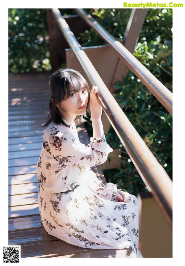 A woman in a white dress sitting on a wooden bridge.