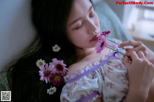 A woman sitting on a bed holding a bouquet of flowers.