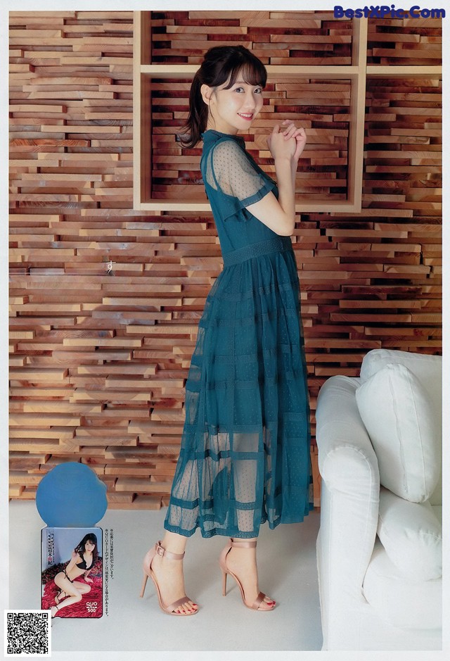 A woman in a blue dress standing in front of a white couch.