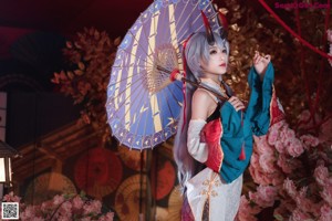 A woman in a costume sitting on a bench with an umbrella.