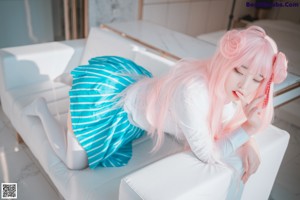 A woman with pink hair sitting on a bed.