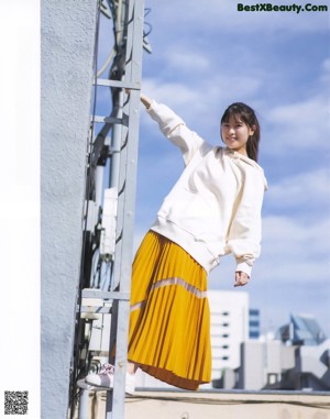 A woman in a white sweatshirt and yellow pleated skirt.