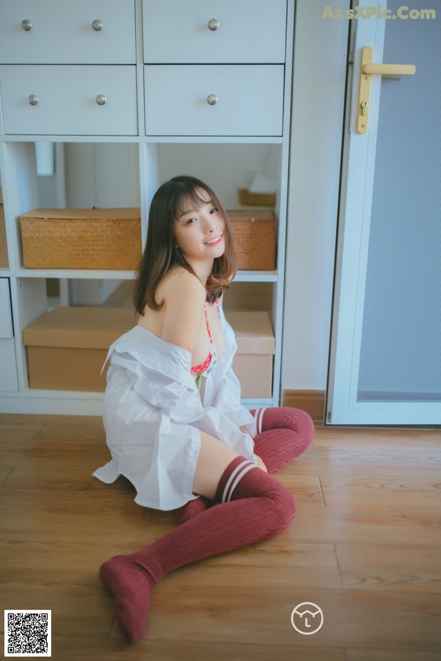 A woman sitting on the floor in a white shirt and red stockings.