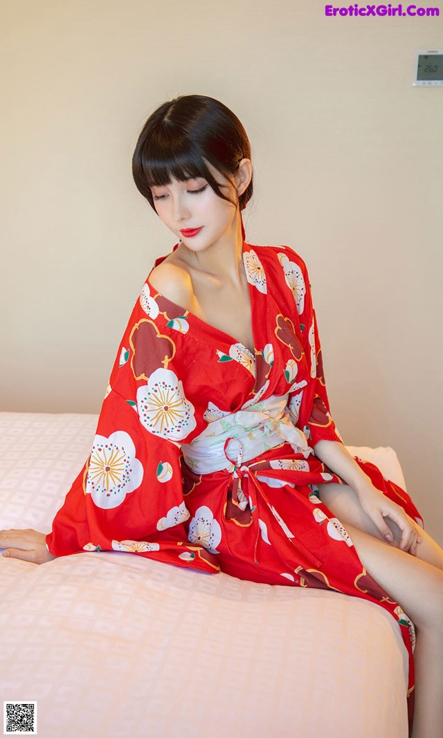 A woman in a red kimono sitting on a bed.