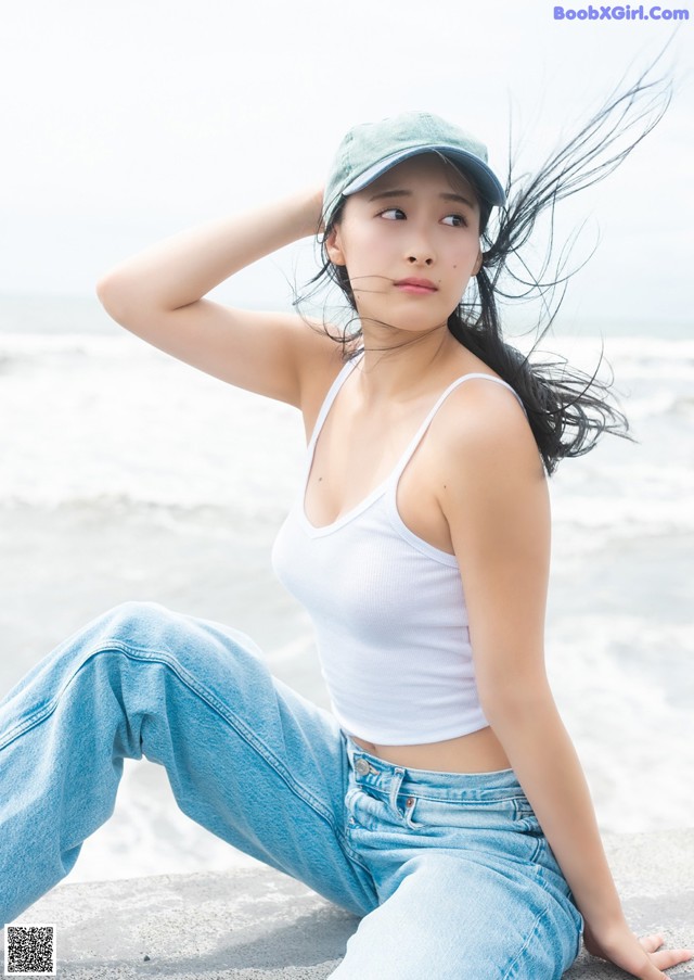 A woman sitting on a rock by the ocean wearing a hat.