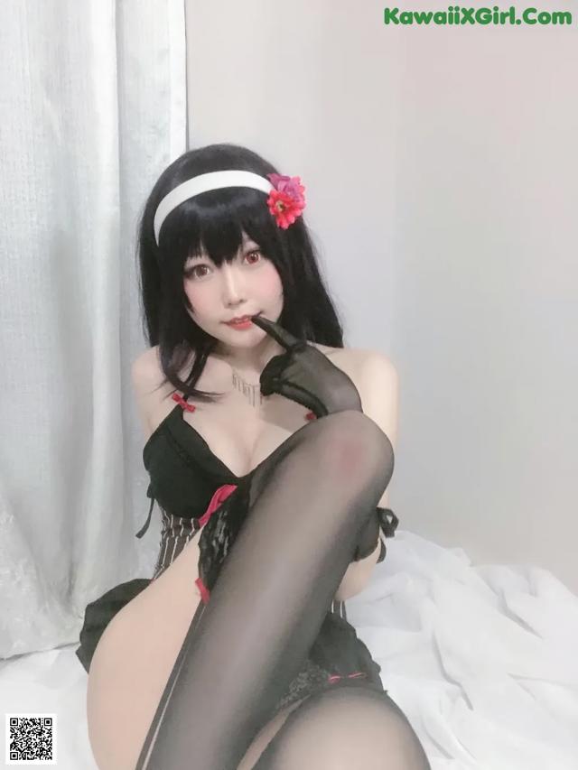 A woman in a black lingerie and stockings sitting on a bed.