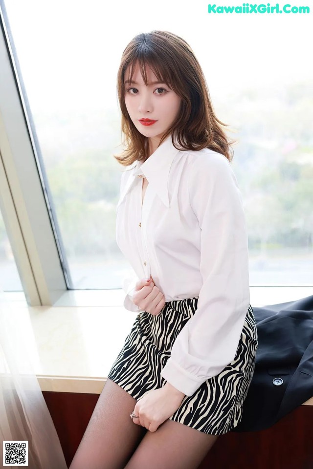 A woman in a white shirt and zebra print skirt sitting on a window sill.