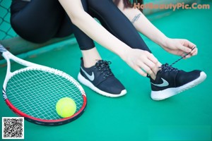 A woman sitting on a tennis court holding a tennis ball.