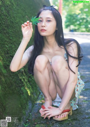 A woman in a bikini leaning against a tree.