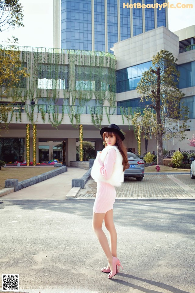 A woman in a pink dress and hat standing in front of a building.