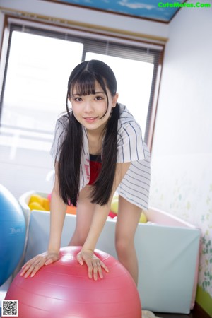 A young woman sitting on a red ball in a room.