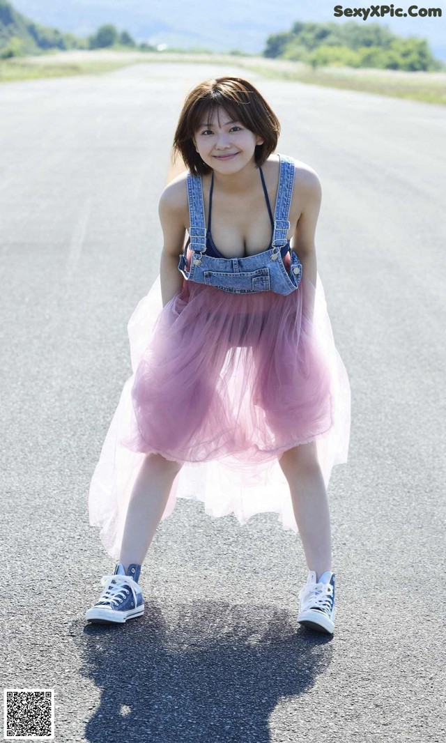 A woman in a pink tulle skirt and denim overalls posing on a road.