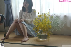 A woman laying on the floor next to a vase of flowers.