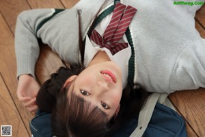 A young woman in a school uniform sitting on the floor.