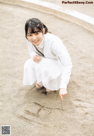 A woman in a white shirt and skirt leaning against a wall.