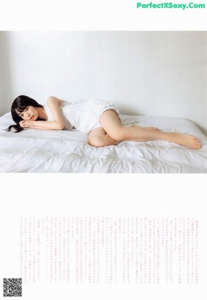 A woman sitting on a bed surrounded by white balloons.