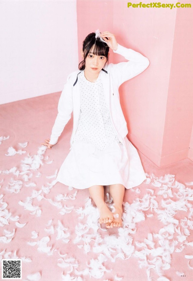 A woman sitting on a pink floor covered in white feathers.